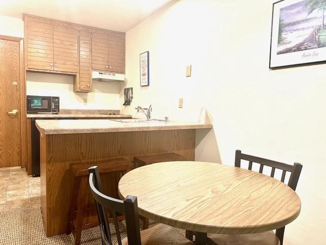 7741 State Highway 42 Unit 105, Egg Harbor, WI 54209 - kitchen with under cabinet range hood, black microwave, a peninsula, light countertops, and a sink