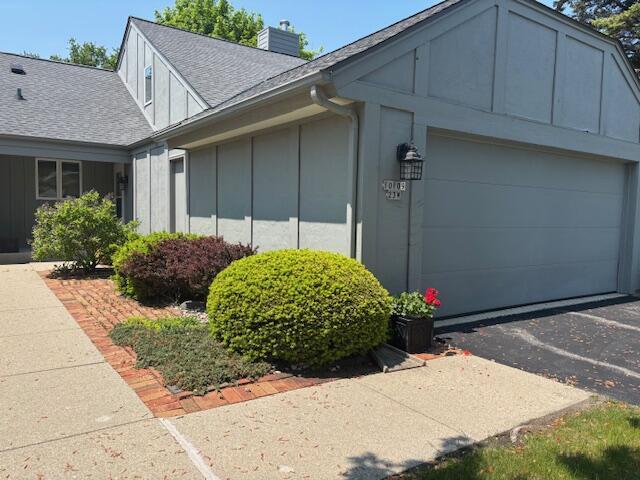 10109 N Gettysburg Ct, Mequon, WI 53092 - view of side of home with board and batten siding, roof with shingles, a chimney, asphalt driveway, and a garage