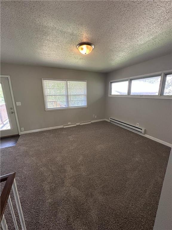 332 E Pleasant Ave, Ellsworth, WI 54011 - empty room featuring a baseboard heating unit, a textured ceiling, dark carpet, and baseboards