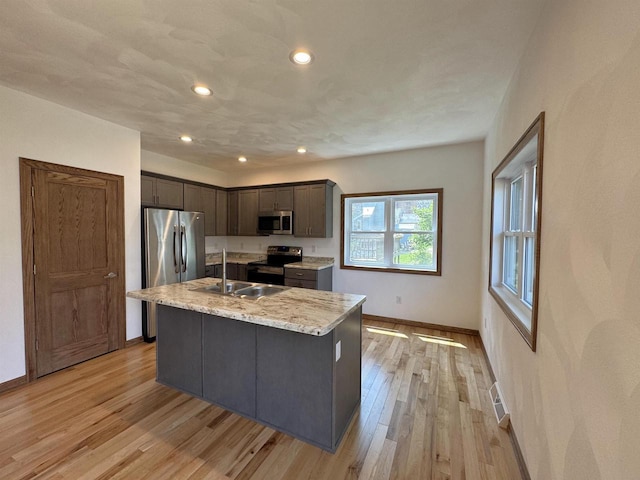 1511 16th Ave, Monroe, WI 53566 - kitchen with stainless steel appliances, a sink, baseboards, light wood-style flooring, and a center island with sink