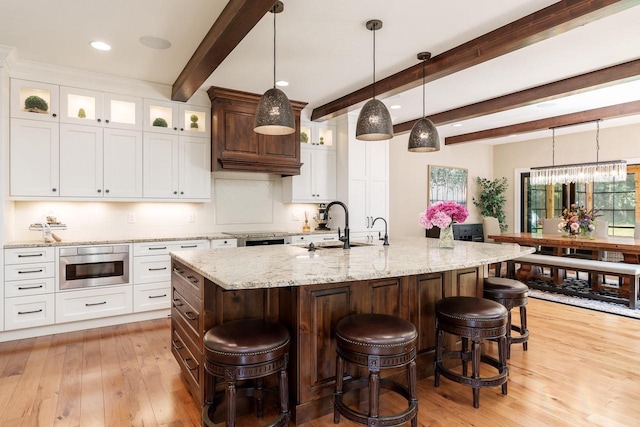 1102 Eldon Way, Edgerton, WI 53534 - kitchen featuring light wood-style flooring, decorative backsplash, a breakfast bar area, glass insert cabinets, and white cabinets