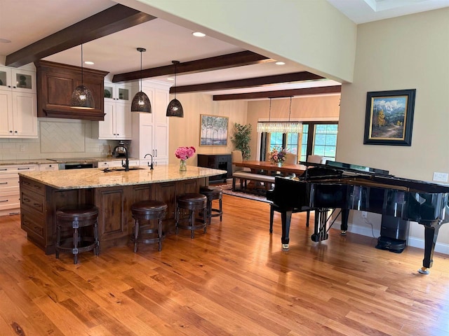 1102 Eldon Way, Edgerton, WI 53534 - kitchen featuring beam ceiling, light wood-style flooring, a breakfast bar area, white cabinets, and decorative backsplash