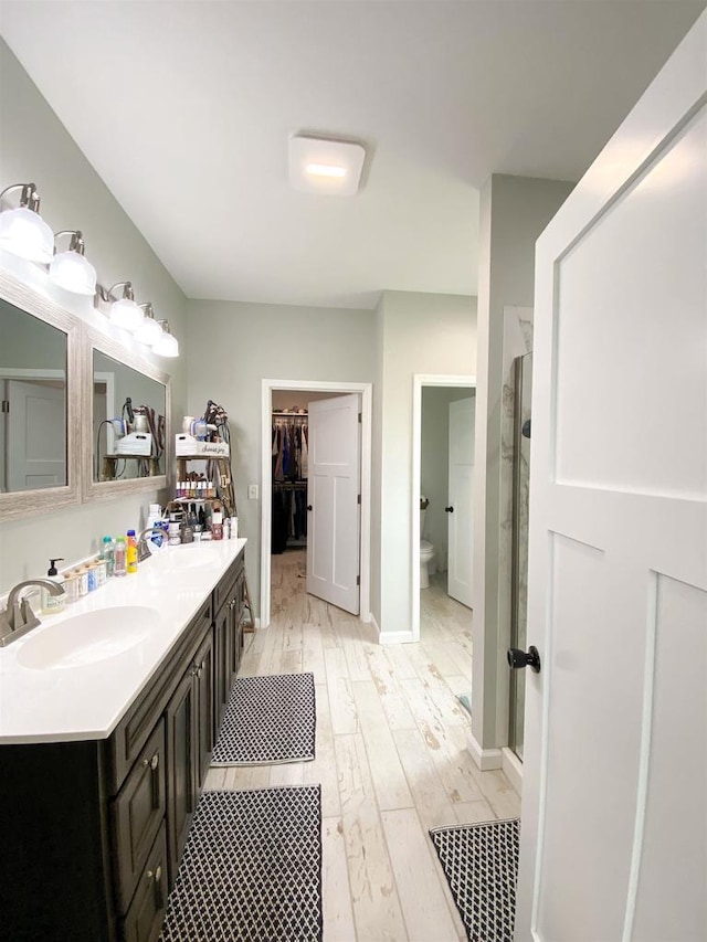 110 Grand St, Highland, WI 53543 - full bathroom featuring wood finished floors, double vanity, toilet, a walk in closet, and baseboards