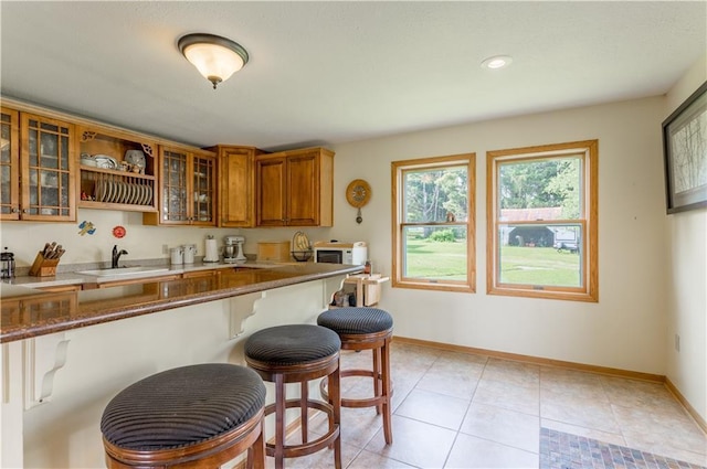 N8355 330th St, Spring Valley, WI 54767 - kitchen with a sink, brown cabinetry, a kitchen breakfast bar, glass insert cabinets, and white microwave