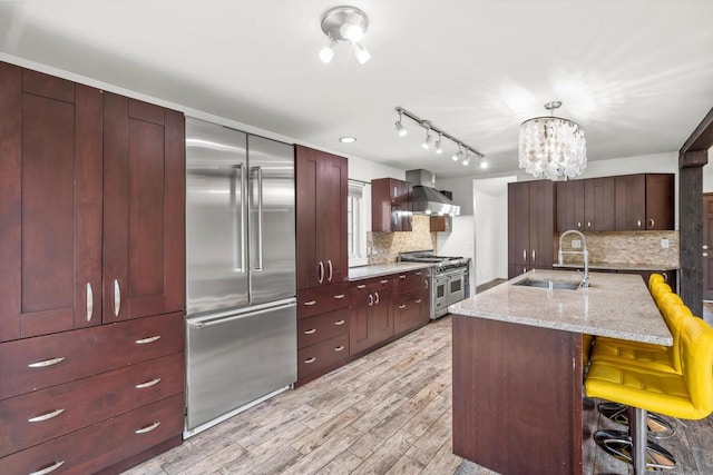 6650 N 114th St, Milwaukee, WI 53224 - kitchen with high quality appliances, a sink, wall chimney exhaust hood, light wood-style flooring, and a kitchen breakfast bar