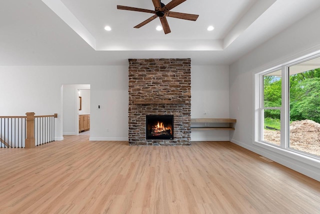 3566 W Hank Ave, De Pere, WI 54115 - unfurnished living room featuring light wood-style floors, a ceiling fan, a tray ceiling, a stone fireplace, and recessed lighting