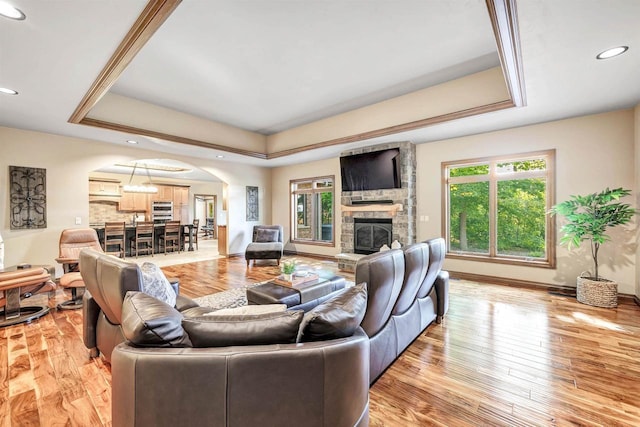 1830 Pine Tree Ct, Luxemburg, WI 54217 - living room with arched walkways, a tray ceiling, light wood-style floors, recessed lighting, and a stone fireplace