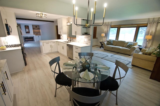 11426 W Woods Rd, Franklin, WI 53132 - dining space with light wood-style floors, a lit fireplace, and a chandelier