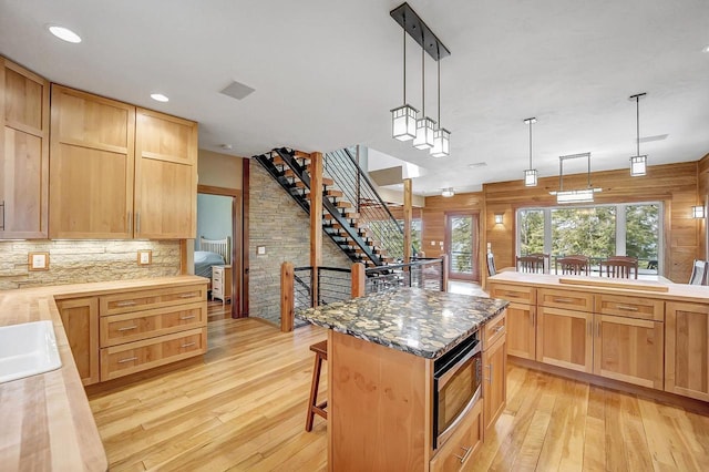 3857 Lake Lucerne Dr, Crandon, WI 54520 - kitchen featuring stainless steel microwave, light wood-style flooring, a kitchen breakfast bar, decorative backsplash, and hanging light fixtures