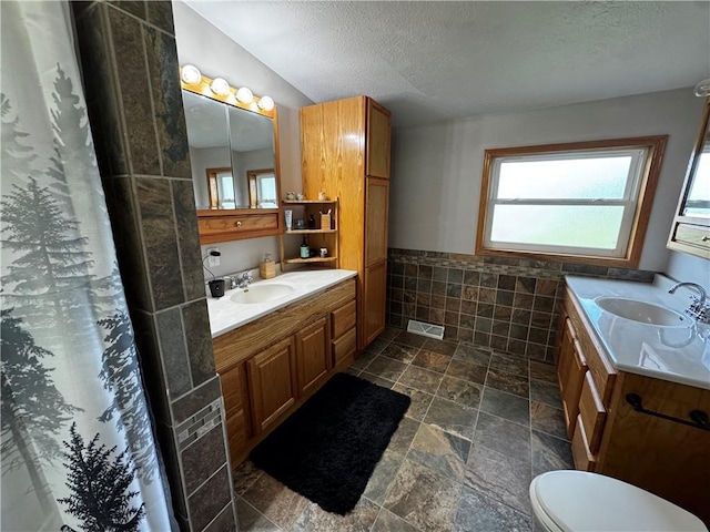 1311 W Northstar Ln, Eau Claire, WI 54703 - bathroom with two vanities, a textured ceiling, stone finish floors, toilet, and tile walls