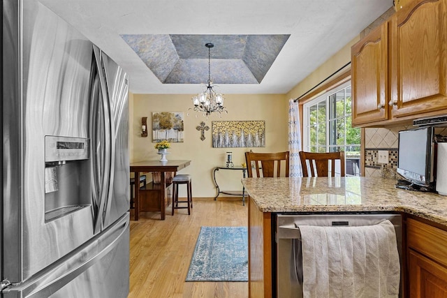831 Browning Dr, Seymour, WI 54165 - kitchen with appliances with stainless steel finishes, a tray ceiling, light wood-style floors, tasteful backsplash, and light stone countertops