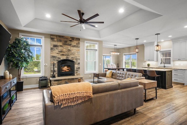 6249 Fountainhead Cir, Deforest, WI 53532 - living area featuring a raised ceiling, a ceiling fan, baseboards, light wood finished floors, and a stone fireplace