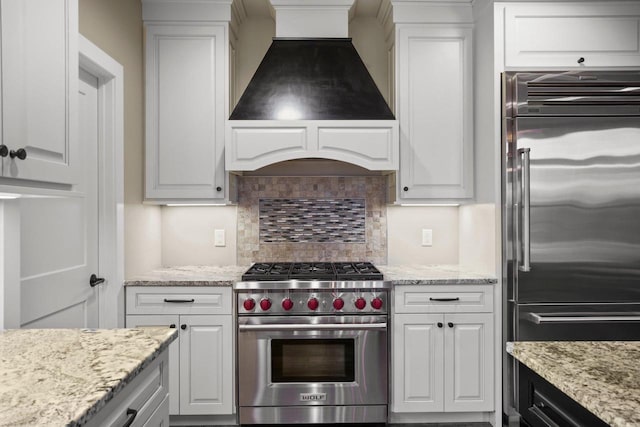 6249 Fountainhead Cir, Deforest, WI 53532 - kitchen featuring premium appliances, custom exhaust hood, white cabinets, tasteful backsplash, and light stone countertops