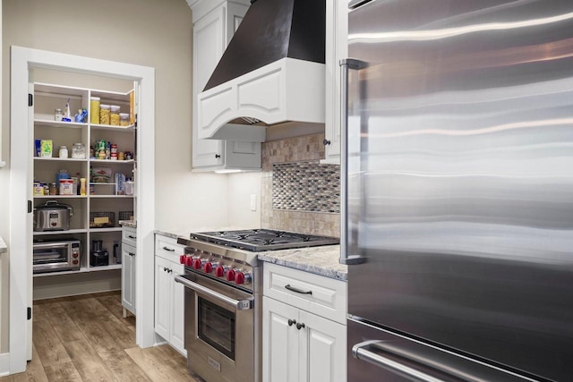 6249 Fountainhead Cir, Deforest, WI 53532 - kitchen with appliances with stainless steel finishes, premium range hood, backsplash, light wood-style flooring, and white cabinetry