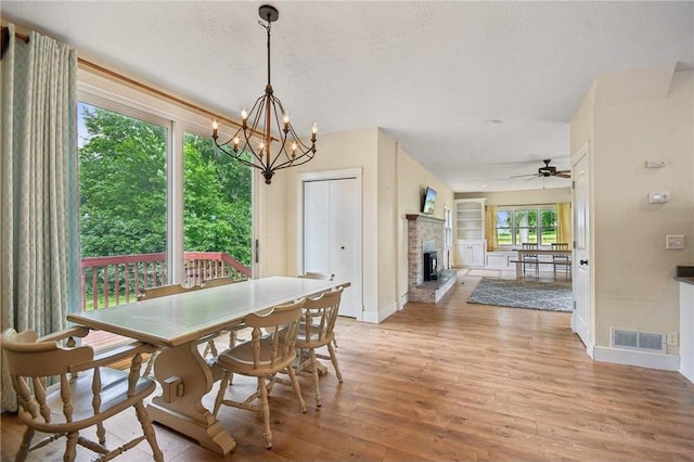2256 40th Ave Unit X, Osceola, WI 54020 - dining space featuring light wood finished floors, ceiling fan, a chandelier, a fireplace with raised hearth, and a textured ceiling