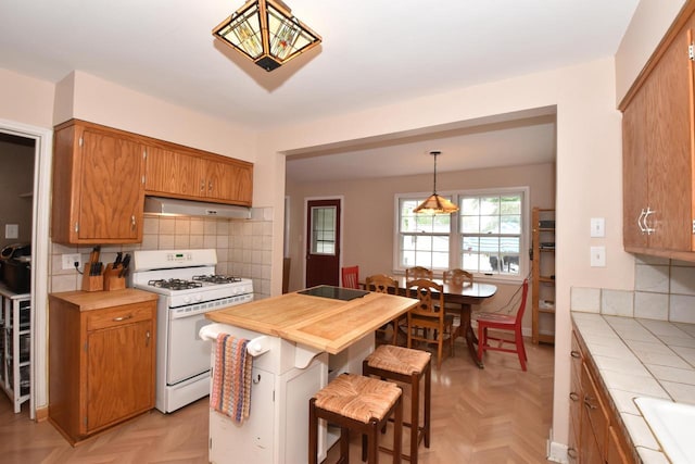 3330 S 47th St, Greenfield, WI 53219 - kitchen featuring white range with gas cooktop, wall chimney range hood, tile counters, brown cabinetry, and tasteful backsplash
