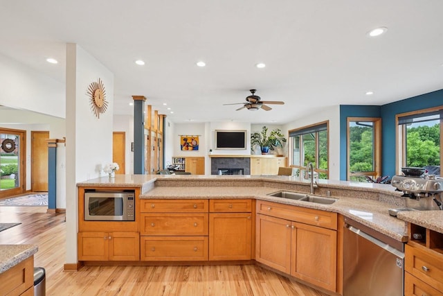 7965 Westhill Cir, Verona, WI 53593 - kitchen with stainless steel appliances, a sink, light wood-style flooring, a fireplace, and light stone countertops