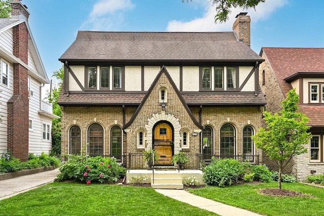 6223 W Wisconsin Ave, Wauwatosa, WI 53213 - tudor house featuring a porch, a front lawn, stucco siding, and a shingled roof