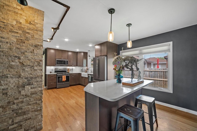 3351 W Vogel Ave, Greenfield, WI 53221 - kitchen featuring stainless steel appliances, light countertops, light wood-style floors, hanging light fixtures, and a kitchen breakfast bar