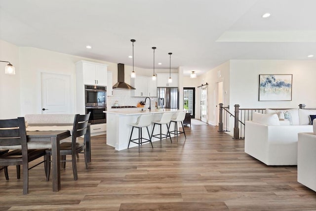 1386 Overlook Cir, Hartland, WI 53029 - kitchen featuring stainless steel appliances, wall chimney exhaust hood, open floor plan, wood finished floors, and tasteful backsplash