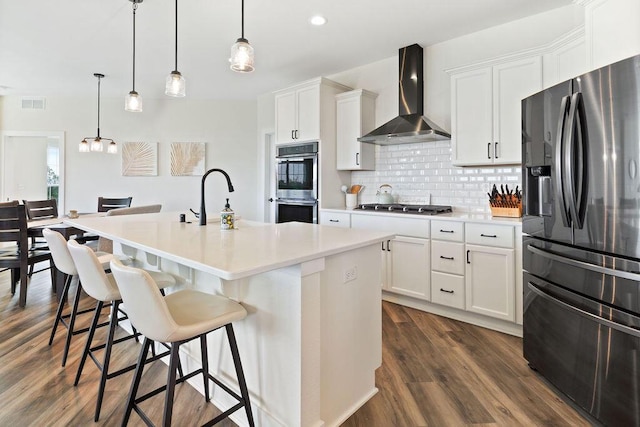 1386 Overlook Cir, Hartland, WI 53029 - kitchen featuring appliances with stainless steel finishes, wall chimney exhaust hood, tasteful backsplash, a center island with sink, and white cabinetry