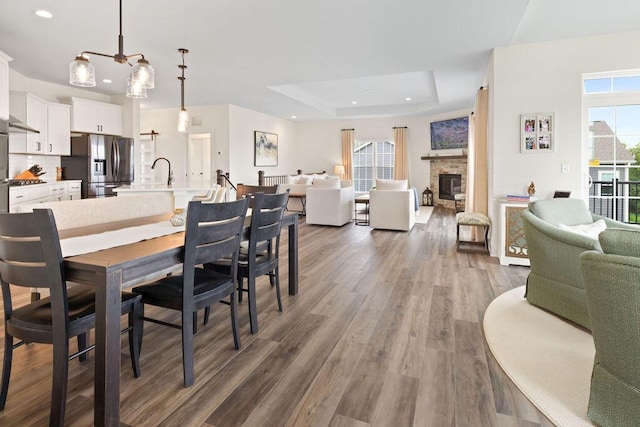 1386 Overlook Cir, Hartland, WI 53029 - dining room featuring plenty of natural light, a tray ceiling, recessed lighting, wood finished floors, and a fireplace