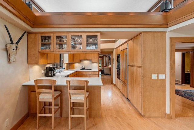 1225 W Cedar St, Appleton, WI 54914 - kitchen with a peninsula, light countertops, light wood-style floors, brown cabinets, and glass insert cabinets