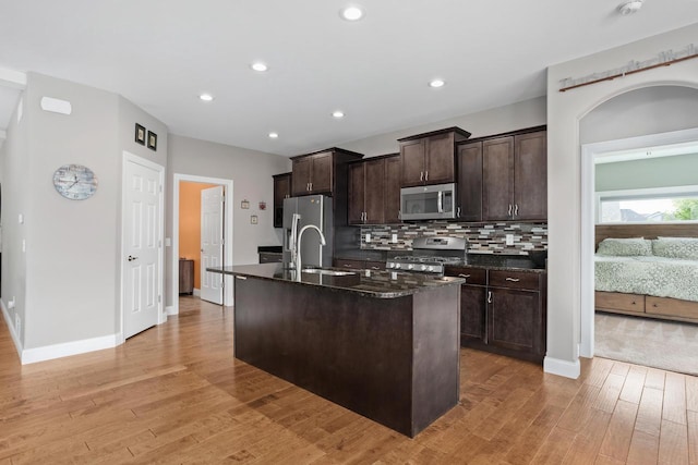 4790 Innovation Dr, Deforest, WI 53532 - kitchen with appliances with stainless steel finishes, light wood-style floors, an island with sink, dark brown cabinets, and tasteful backsplash