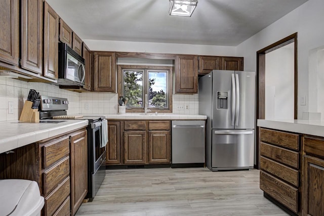 N9695 Willard Rd, Berlin, WI 54923 - kitchen featuring appliances with stainless steel finishes, tile counters, backsplash, light wood-style flooring, and dark brown cabinetry