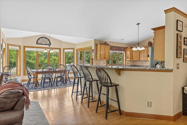 110 Chestnut Way, North Prairie, WI 53153 - kitchen with vaulted ceiling, a chandelier, light wood finished floors, a breakfast bar, and decorative light fixtures