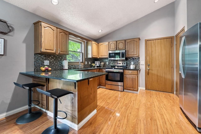 1434 Alcan Dr, Menasha, WI 54952 - kitchen with appliances with stainless steel finishes, a peninsula, light wood finished floors, vaulted ceiling, and tasteful backsplash