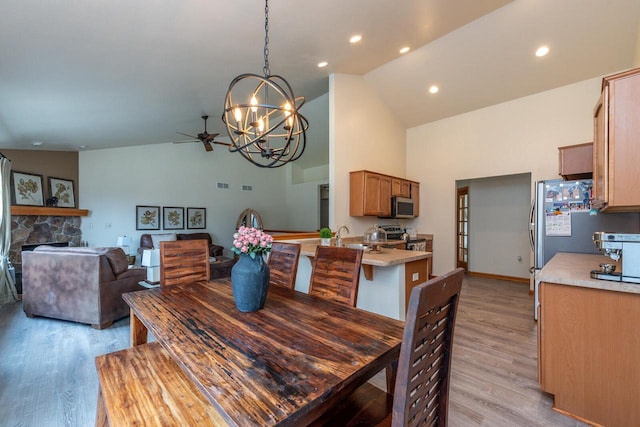 431 Thurow Dr, Oconomowoc, WI 53066 - dining area with light wood finished floors, a chandelier, a fireplace, high vaulted ceiling, and a ceiling fan