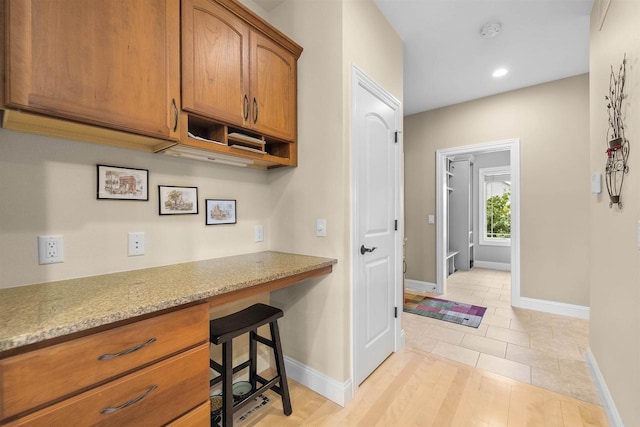 7131 Caneel Trl, Middleton, WI 53562 - kitchen featuring brown cabinets, built in study area, a kitchen breakfast bar, recessed lighting, and light stone countertops