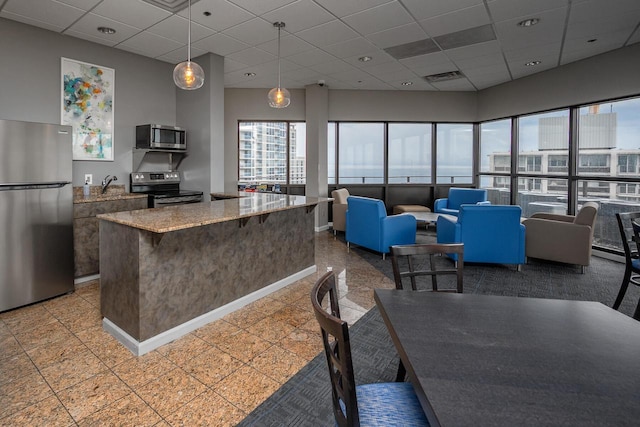 1633 N Prospect Ave Unit 18F, Milwaukee, WI 53202 - kitchen featuring stainless steel appliances, a drop ceiling, hanging light fixtures, a kitchen island, and light stone countertops