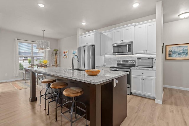 N9225 Constellation Dr, Appleton, WI 54915 - kitchen featuring stainless steel appliances, a kitchen bar, a kitchen island with sink, light wood-style flooring, and white cabinetry