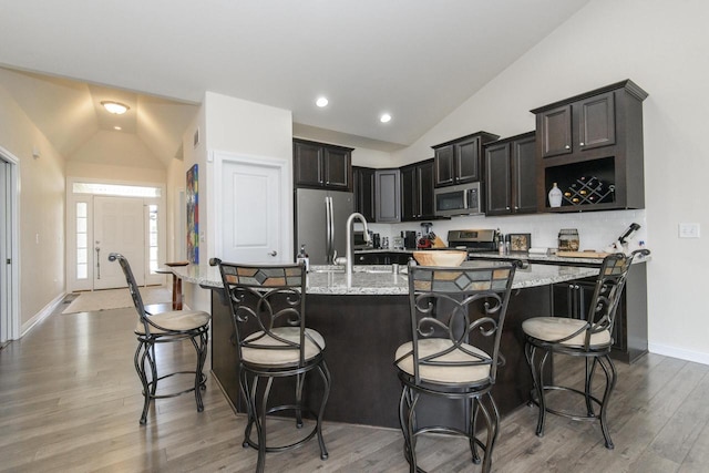 12907 78th Pl, Bristol, WI 53104 - kitchen with vaulted ceiling, stainless steel appliances, light wood-style flooring, light stone countertops, and a breakfast bar area