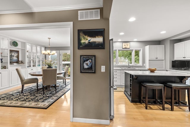 544 Maple Bluff Rd, Stevens Point, WI 54482 - kitchen with ornamental molding, a chandelier, light wood-style flooring, white cabinets, and a kitchen bar