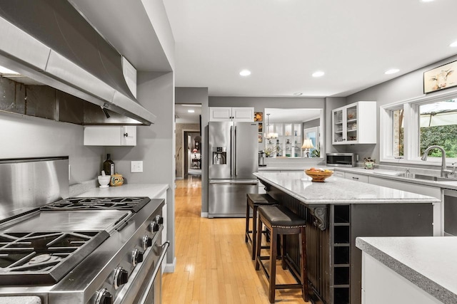 544 Maple Bluff Rd, Stevens Point, WI 54482 - kitchen featuring stainless steel appliances, wall chimney range hood, white cabinetry, a breakfast bar area, and light wood-type flooring