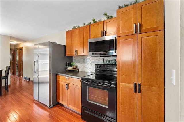 1516 Mitscher Ave, Eau Claire, WI 54701 - kitchen with appliances with stainless steel finishes, wood finished floors, decorative backsplash, dark countertops, and brown cabinetry