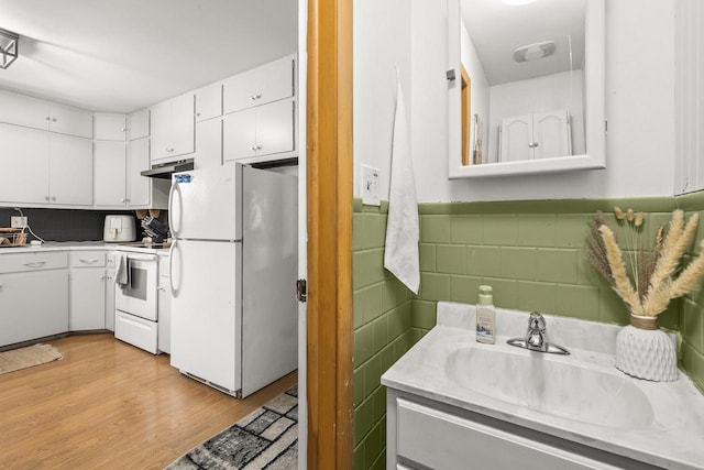 551 Market Ave, Port Edwards, WI 54469 - kitchen with white appliances, under cabinet range hood, white cabinetry, light countertops, and light wood-style flooring