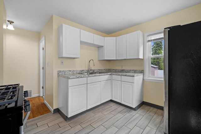2225 Shoop St, Racine, WI 53404 - kitchen featuring freestanding refrigerator, black range with gas cooktop, wood finish floors, white cabinetry, and light stone countertops