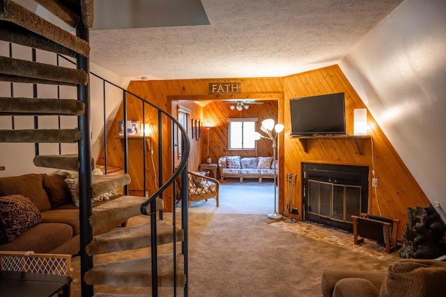 N8244 Woodland Trl, New Lisbon, WI 53950 - carpeted living room with wooden walls, stairs, a fireplace with flush hearth, a ceiling fan, and a textured ceiling