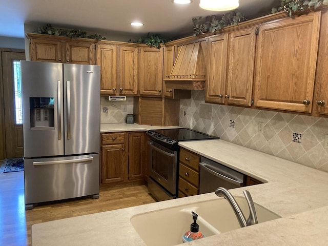 3988 S 18th St, Sheboygan, WI 53081 - kitchen featuring appliances with stainless steel finishes, custom range hood, light countertops, light wood-style floors, and brown cabinetry