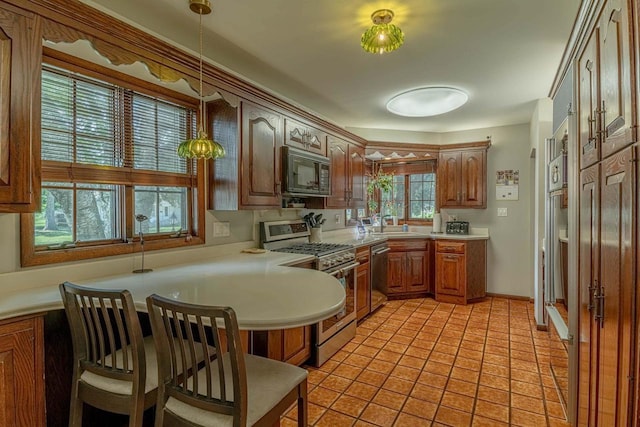 1329 23rd Ave, Monroe, WI 53566 - kitchen featuring appliances with stainless steel finishes, light countertops, a peninsula, decorative light fixtures, and brown cabinetry