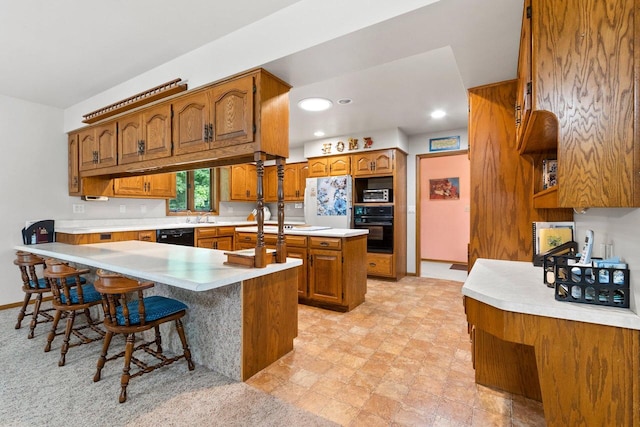 2929 Brunner Rd, Manitowoc, WI 54220 - kitchen featuring black appliances, brown cabinetry, a peninsula, light countertops, and a kitchen breakfast bar