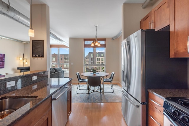 1541 N Jefferson St Unit 408, Milwaukee, WI 53202 - kitchen with brown cabinetry, stainless steel appliances, light wood finished floors, decorative light fixtures, and dark stone countertops