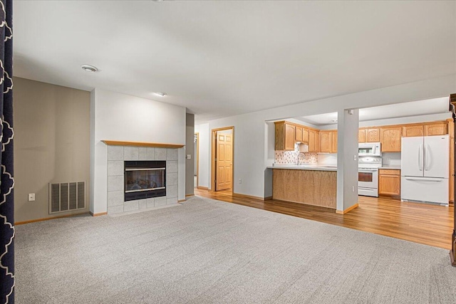 677 Wood River Ct, West Bend, WI 53095 - unfurnished living room with a tile fireplace, light carpet, and light wood finished floors