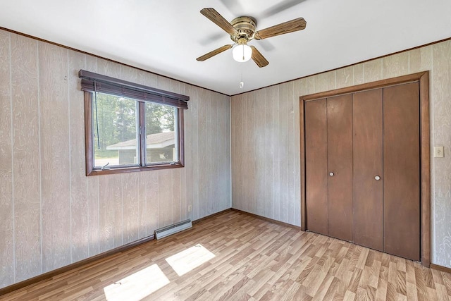 11975 E Anderson Lake Dr, Suring, WI 54174 - unfurnished bedroom featuring baseboard heating, light wood-style flooring, a closet, wood walls, and ceiling fan