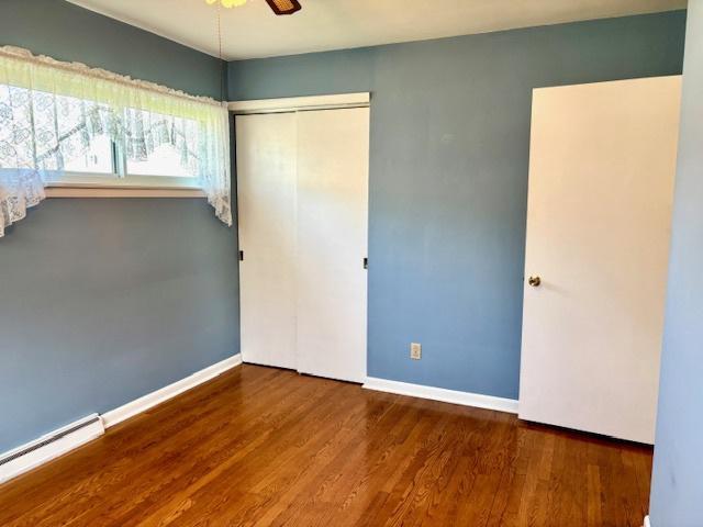 1710 N 25th St, Sheboygan, WI 53081 - unfurnished bedroom featuring a baseboard heating unit, a closet, wood finished floors, and ceiling fan