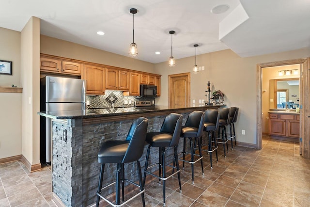 6507 Willow Ct, Waterford, WI 53185 - kitchen with black microwave, a kitchen breakfast bar, freestanding refrigerator, tasteful backsplash, and decorative light fixtures